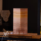 Rectangular Miami Sunset Onyx table lamp with warm horizontal banded patterns in shades of pink, orange, and brown, sitting on a wooden surface with a dark background.