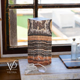Rectangular onyx table lamp with layered brown, black, and cream natural stone patterns, placed on a marble surface in front of a multi-pane window.