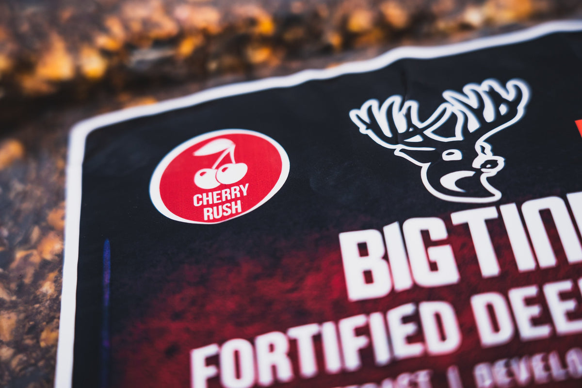 Close-up of product packaging showing a red circle with cherry icon labeled 'Cherry Rush' and a stylized deer head above the bold white text 'Big Tine Fortified Deer' on a dark background.