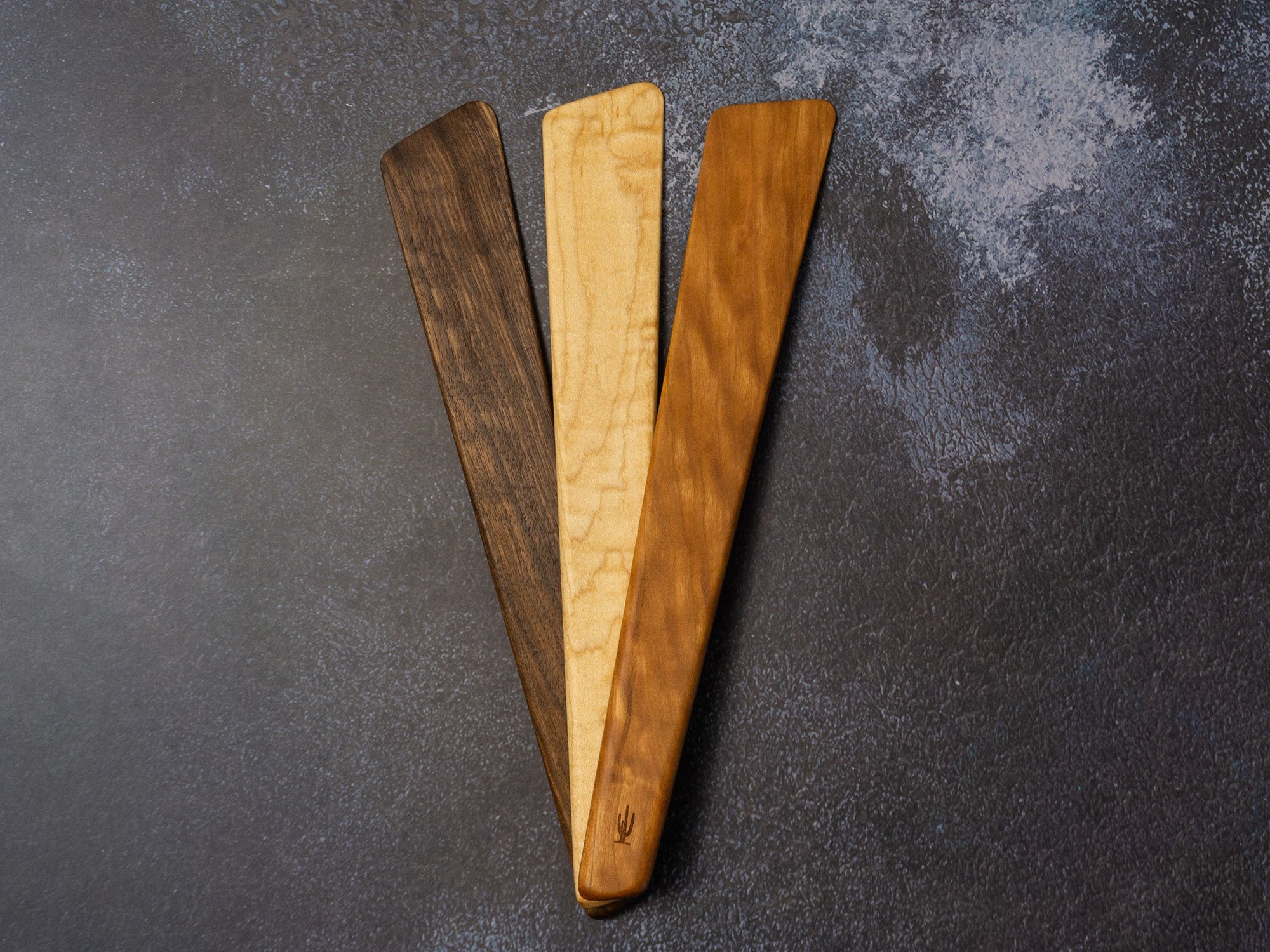 Wooden spatula resting on a dark textured surface, showing wood grain and slender shape