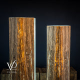 Pair of tall, rectangular onyx floor lamps with vertical brown and amber striations glowing softly against a dark background on wooden blocks.