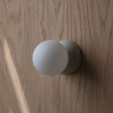 Round matte white wall sconce with spherical light fixture mounted on light wood grain wall, casting a soft shadow to the right.