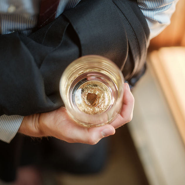 Clear glass tumbler held in hand, featuring a gold and brown textured dinosaur bone shard embedded at the bottom center.
