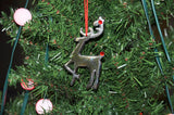 Silver reindeer Christmas ornament with red nose and red eye hanging on a green pine tree branch decorated with round pink lights.