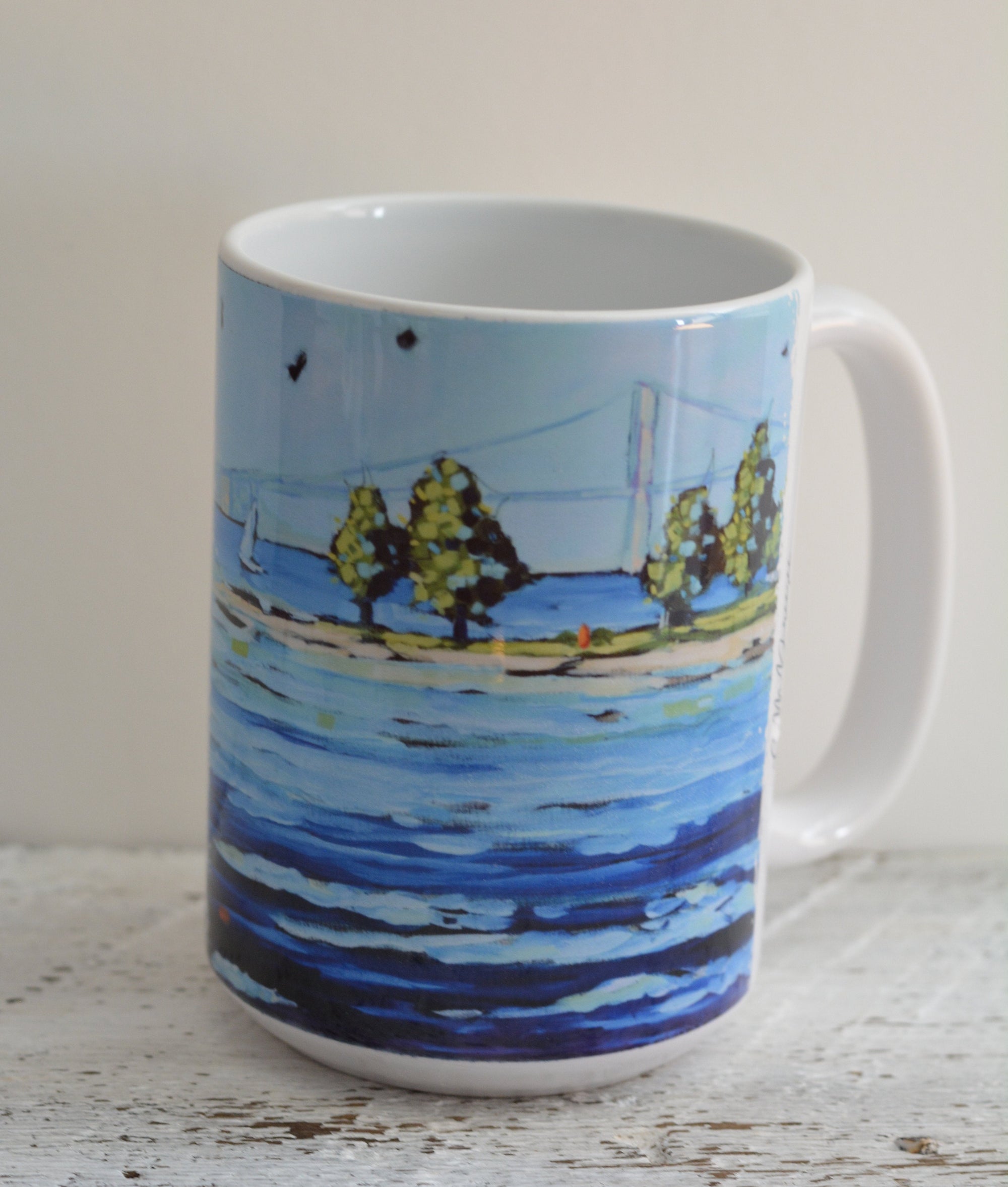 Ceramic mugs and stainless steel tumbler featuring Sailing at Mackinac Bridge artwork by Christi Dreese arranged on a tabletop