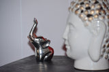 Small silver-finished elephant figurine with raised trunk holding a delicate ring, positioned on a dark surface beside a white Buddha head sculpture.