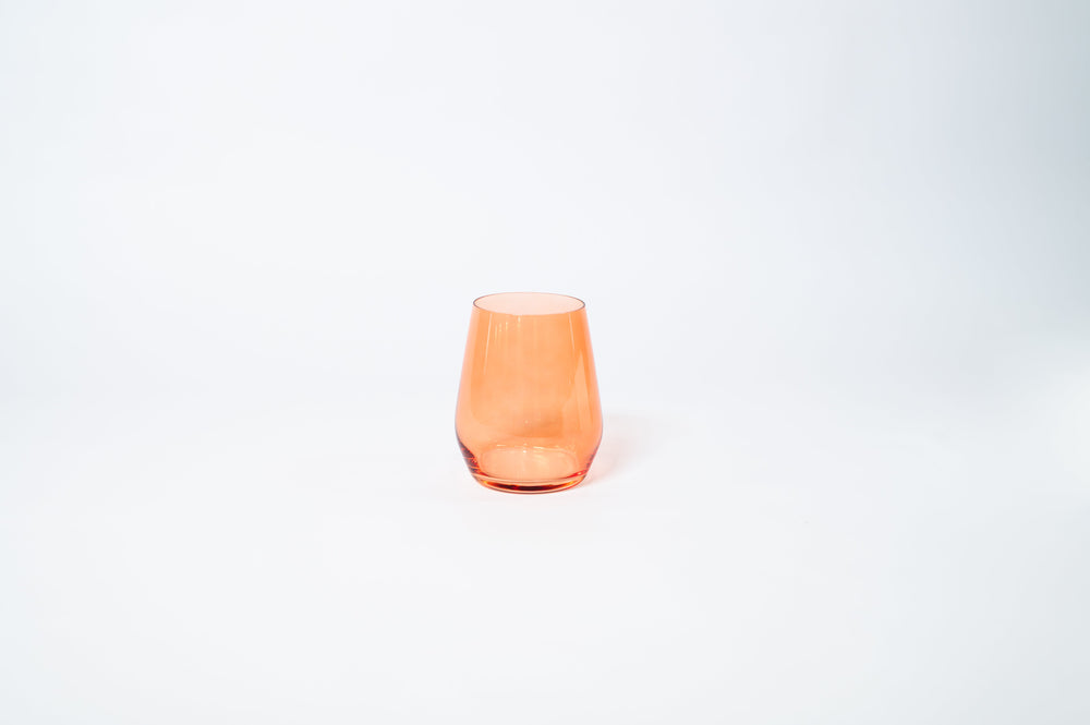 Stemless wine glass in Aperol orange color placed on a light surface with warm lighting