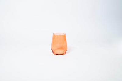 Stemless wine glass in Aperol orange color placed on a light surface with warm lighting