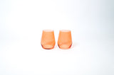 Two short, translucent orange wine glasses with rounded bases side by side on a white background.