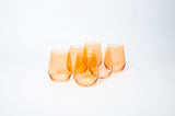 Five stemless wine glasses in translucent orange with gently curved sides, arranged closely on a white background.