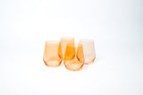 Four stemless wine glasses in varying shades of translucent orange with gently curved sides and slightly tapered rims, set against a white background.