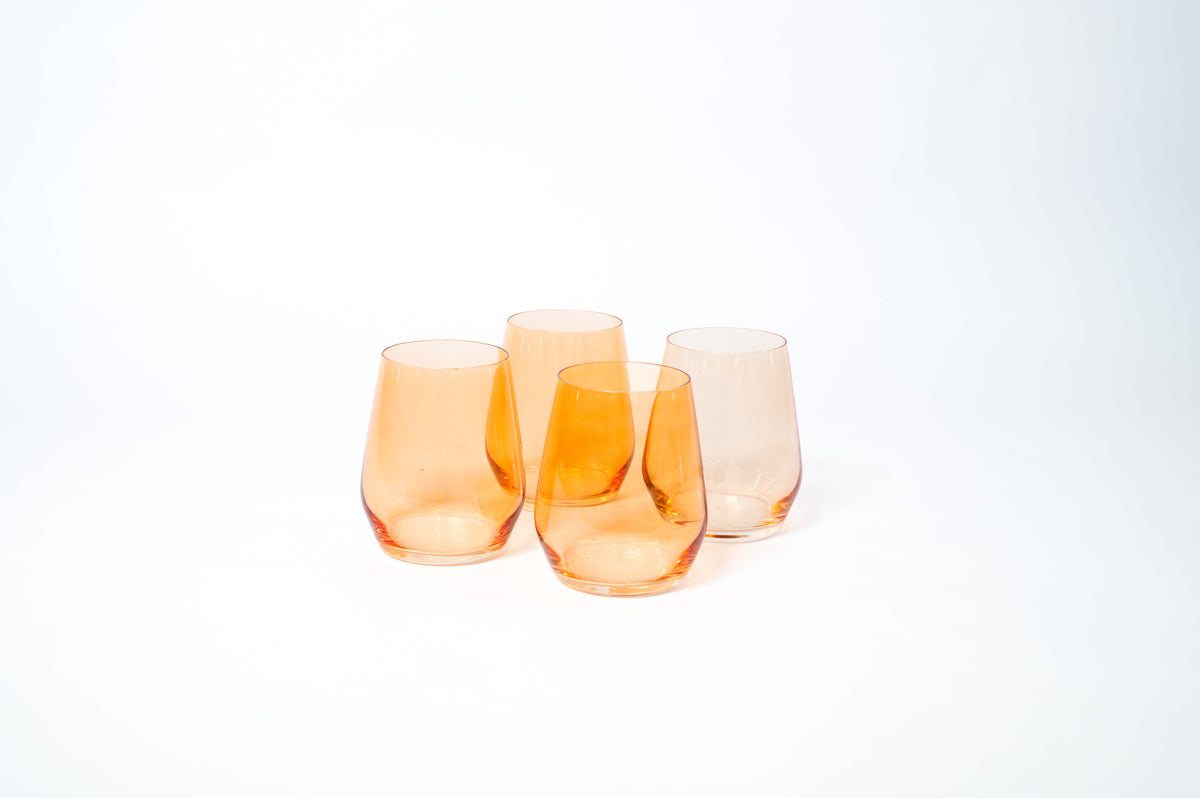 Four stemless wine glasses in varying shades of translucent orange with gently curved sides and slightly tapered rims, set against a white background.