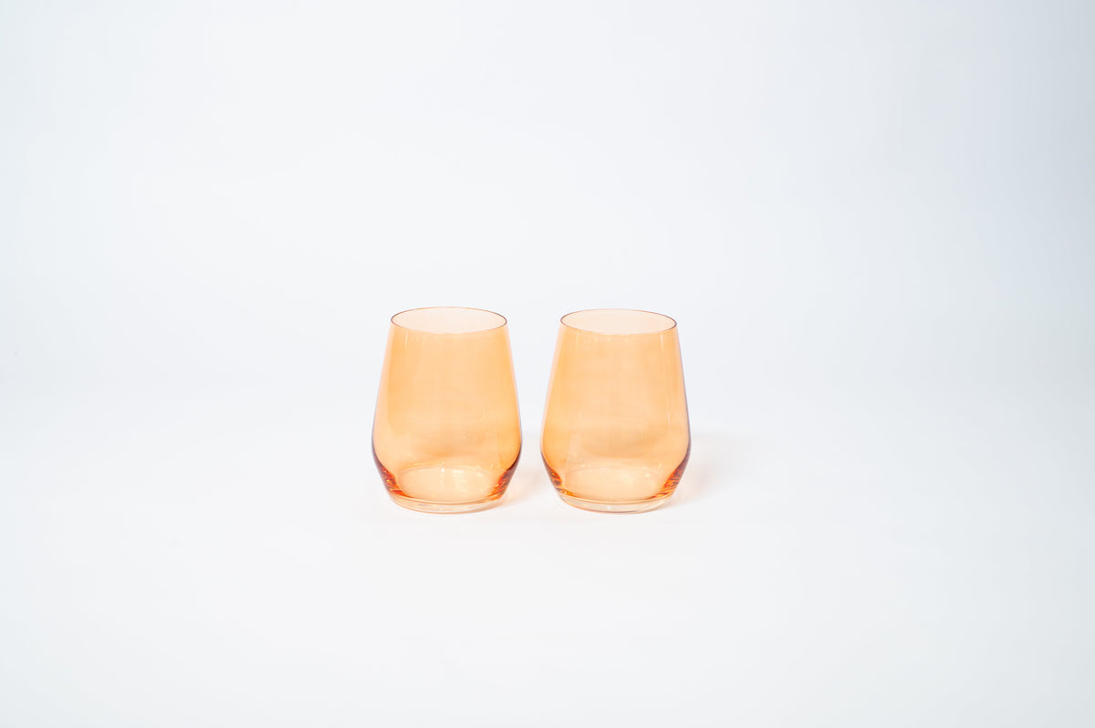 Two translucent orange stemless wine glasses with smooth, rounded bodies and slightly tapered tops, placed side by side on a plain white background.