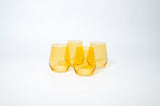 Four stemless wine glasses in translucent sunshine yellow arranged in a tight cluster on a white background with soft shadows.
