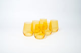 Set of six translucent sunshine yellow wine glasses with a rounded base and no stems, arranged closely on a white surface with soft shadows.