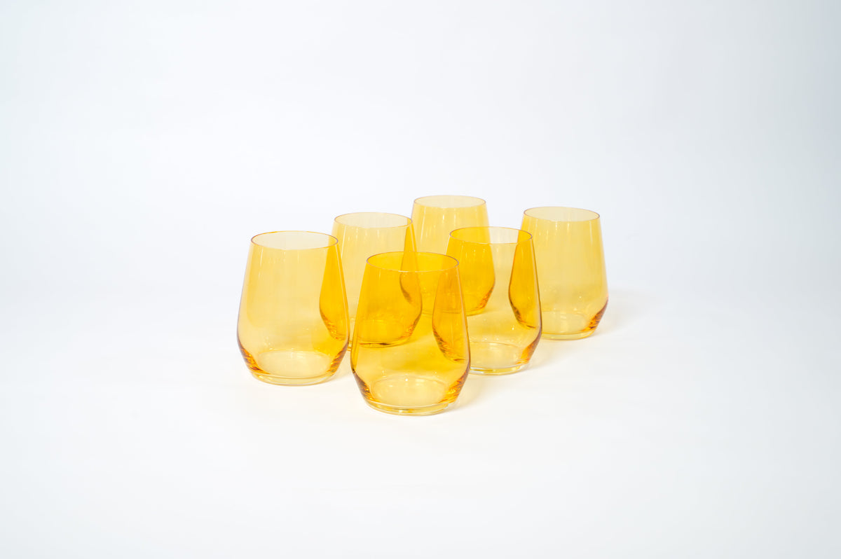 Set of six translucent sunshine yellow wine glasses with a rounded base and no stems, arranged closely on a white surface with soft shadows.