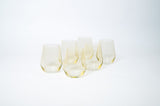 Six stemless wine glasses with a subtle lemon yellow tint arranged in a loose group on a white background.