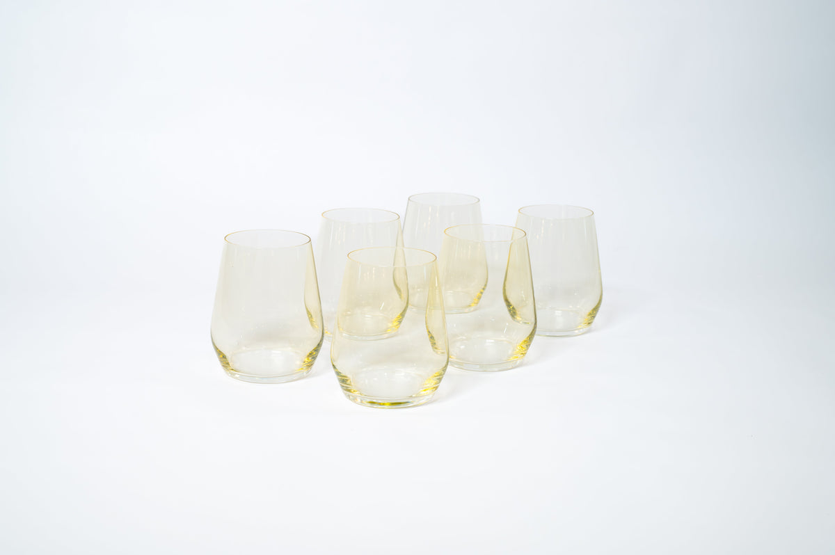 Six stemless wine glasses with a subtle lemon yellow tint arranged in a loose group on a white background.