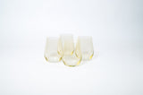 Set of five translucent stemless wine glasses with a subtle lemon yellow tint arranged on a white surface against a white background.