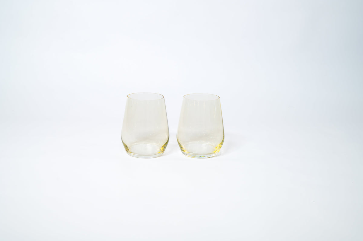 Two stemless wine glasses with a subtle lemon drop yellow tint, displayed side by side on a plain white background with soft lighting.