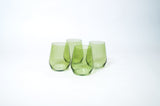 Set of four translucent matcha green stemless wine glasses with gently curved sides, arranged closely on a white surface.