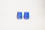 Two indigo-colored glass tumblers with slightly rounded sides, shown side by side on a plain white background.