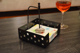 Black metal napkin holder with star-shaped cutouts and an American football-shaped silver handle, holding colorful starburst patterned napkins on a dark wood table.