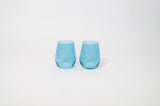 Two translucent blue wine glasses with a soft, rounded shape and slight taper, set side-by-side on a plain white surface.