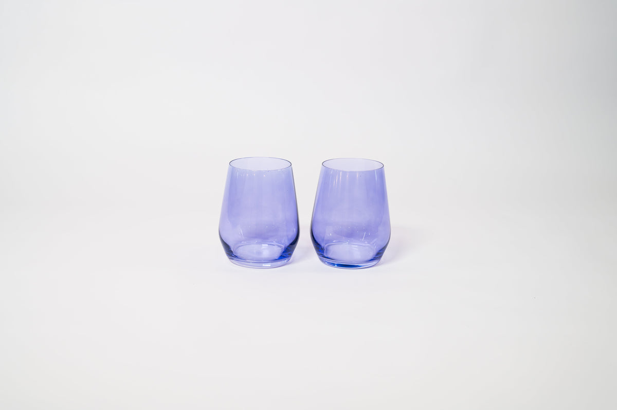 Two translucent stemless wine glasses in a soft periwinkle purple hue, placed side by side on a plain white surface.