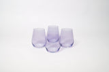 Set of four translucent lavender stemless wine glasses with rounded bodies and slightly tapered tops arranged in a group on a white background.
