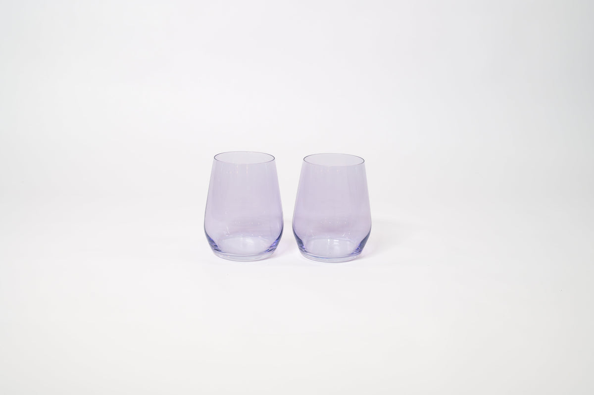 Pair of stemless wine glasses in translucent lavender color with a smooth, curved silhouette, shown side by side on a white background.