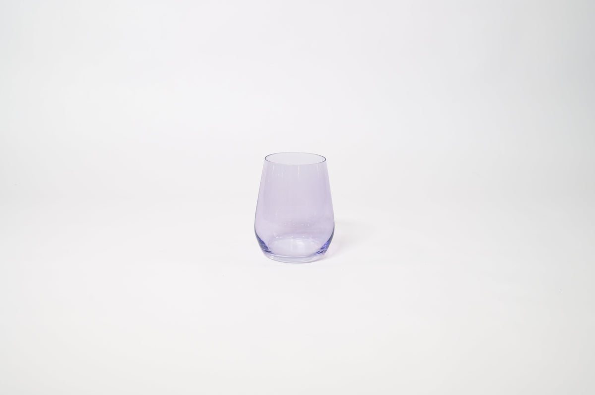 Stemless wine glass with a soft lavender tint holding white wine on a textured surface