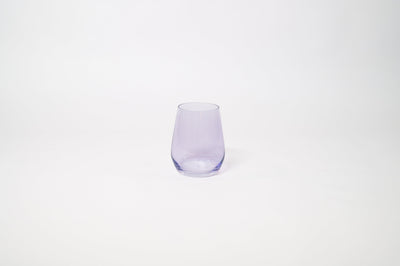 Stemless wine glass with a soft lavender tint holding white wine on a textured surface