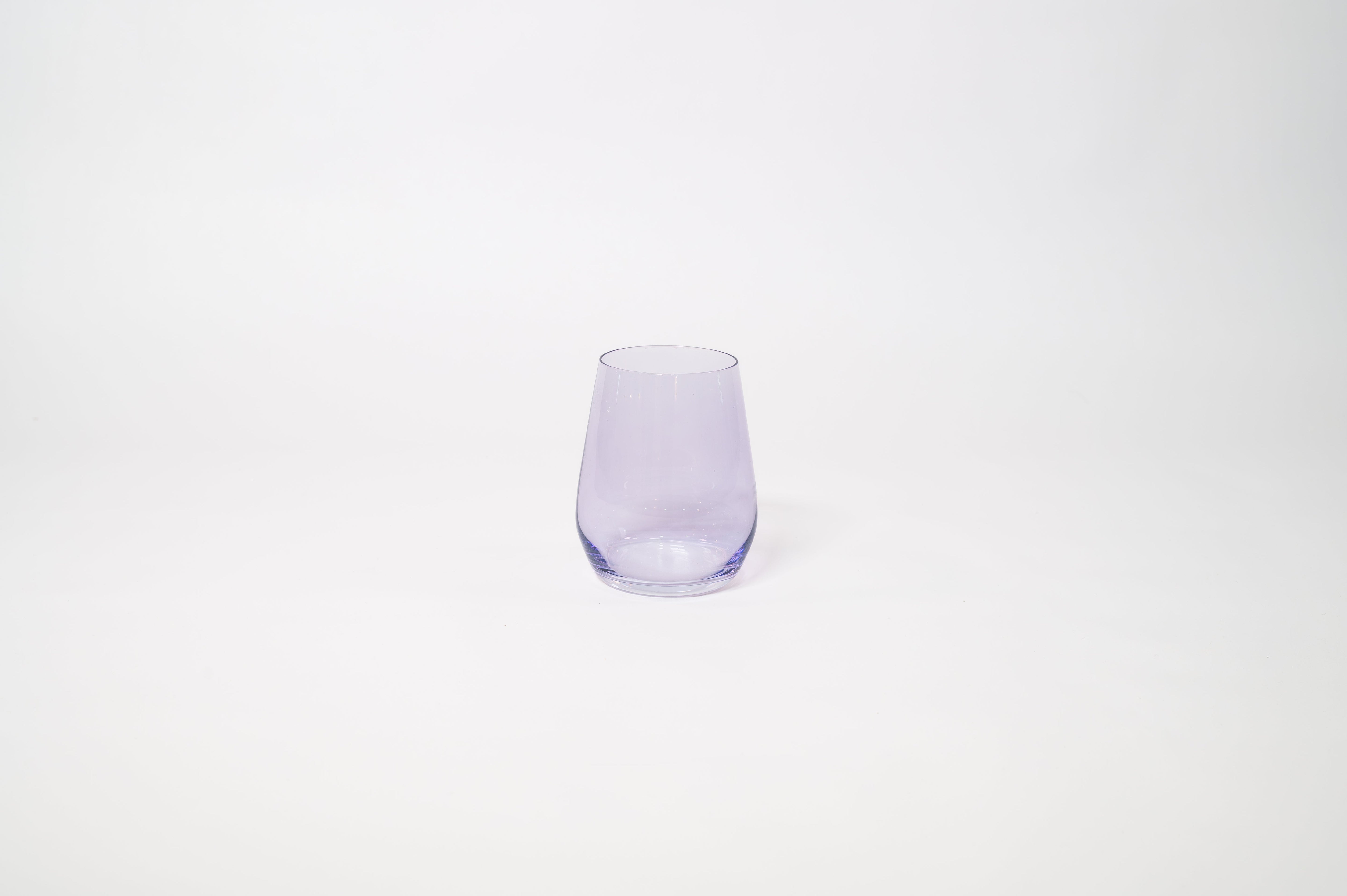 Stemless wine glass with a soft lavender tint holding white wine on a textured surface