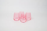 Four stemless wine glasses in translucent bubblegum pink, arranged in a loose cluster on a white surface with soft shadows.