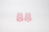 Two translucent bubblegum pink stemless wine glasses with gently angled sides set against a plain white background.