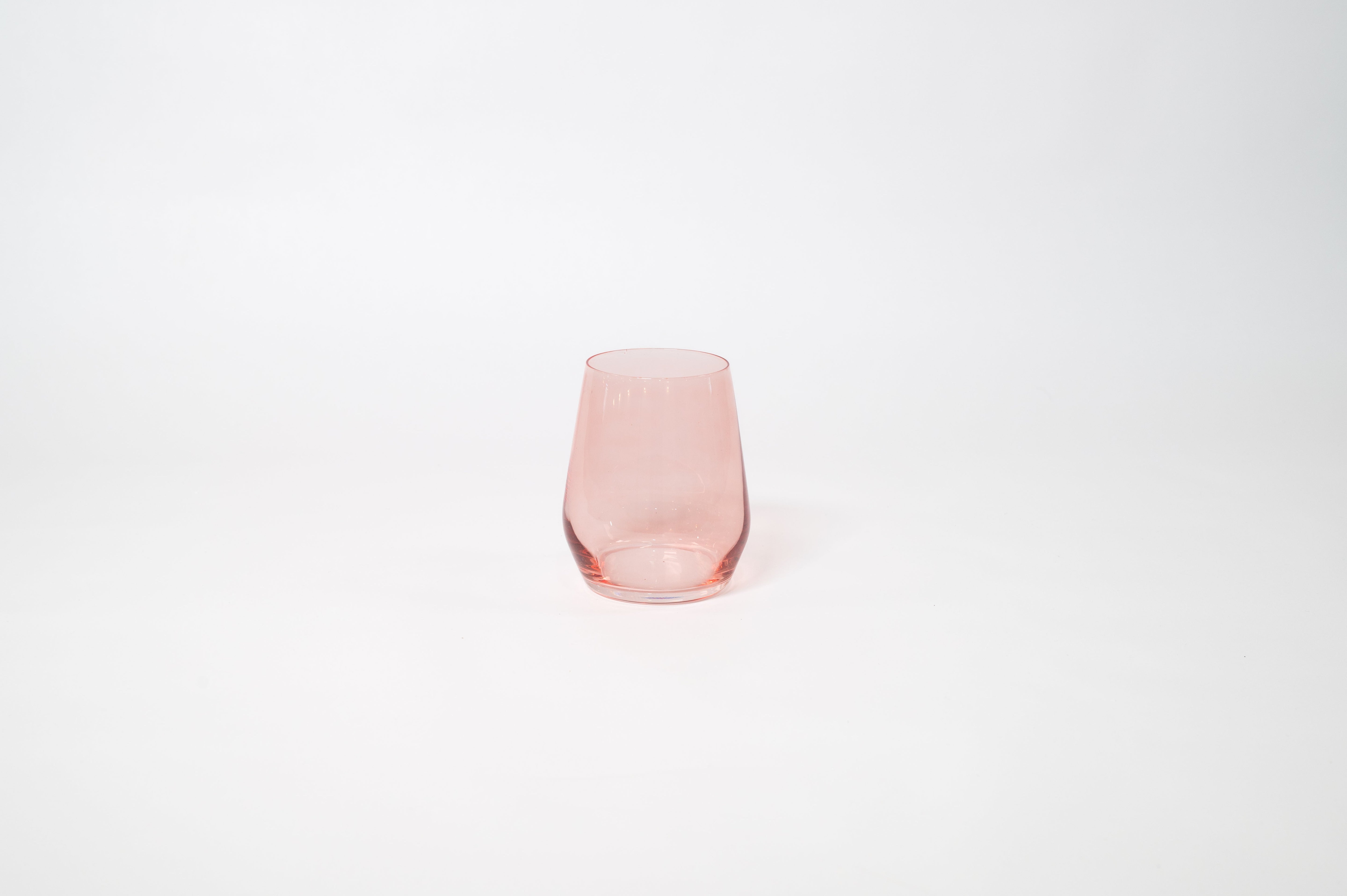 Tickle Me Pink stemless wine glass in soft pastel pink on a wooden surface with greenery in the background