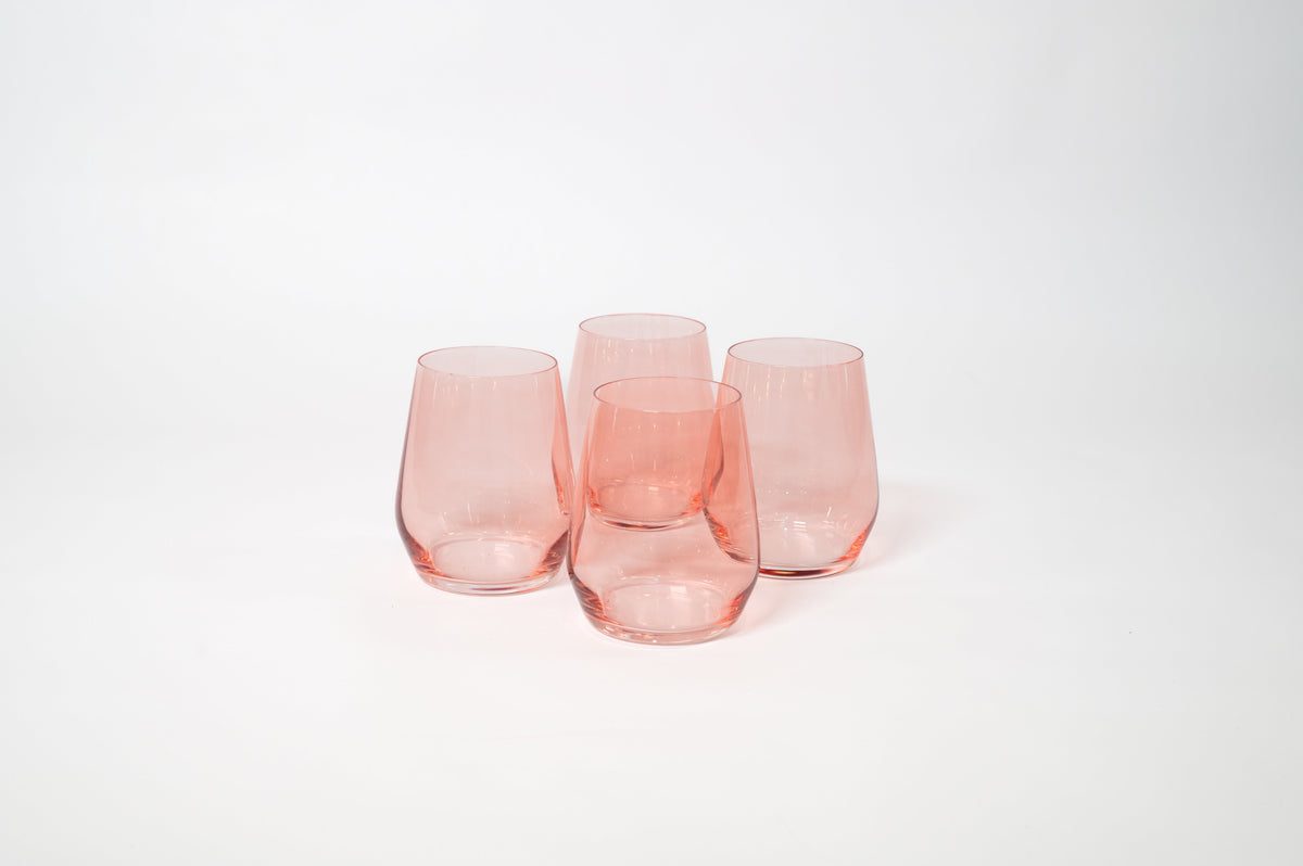 Four translucent pink stemless wine glasses with rounded bases grouped against a plain white background.
