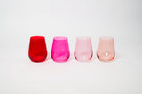 Set of four stemless ombre wine glasses in red, bright pink, light pink, and pale peach arranged in a row against a plain white background.