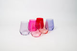 Six stemless colored wine glasses in purple, pink, red, and lavender shades grouped on a white background with a faceted design.