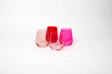 Four stemless ombre wine glasses arranged in shades from dark red to soft pink on a white surface.