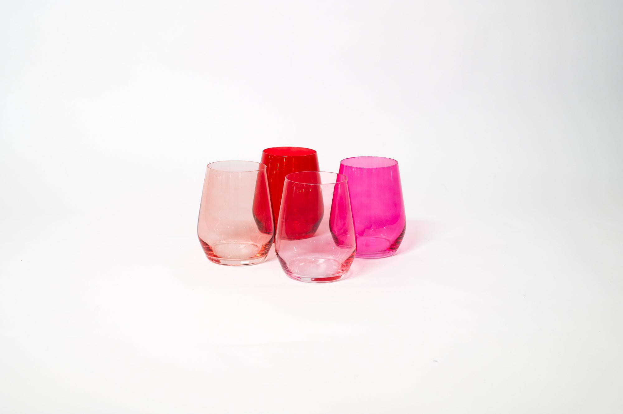 Four stemless ombre wine glasses arranged in shades from dark red to soft pink on a white surface.