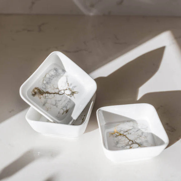 Two white geometric resin jewelry holders with small items inside on a marble surface