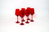 Six transparent cherry red colored stemmed wine glasses grouped closely on a white background, showing their uniform height and rich red hue.