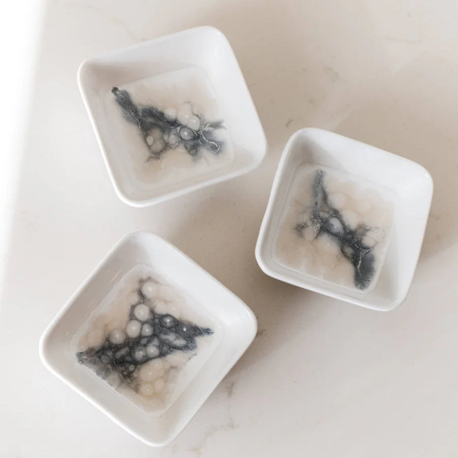 Three small white square resin dishes with black dendritic patterns on a light gray background