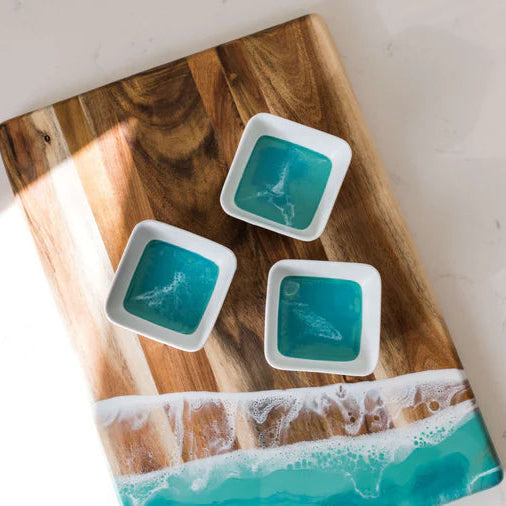 Four small white resin containers with blue substance on a wooden cutting board.