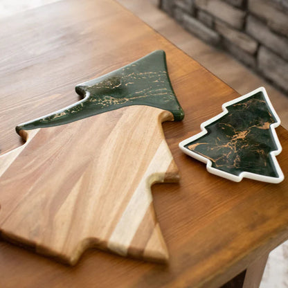 Wooden cutting board shaped like a Christmas tree with a matching green marble-patterned cheese board on a wooden surface.