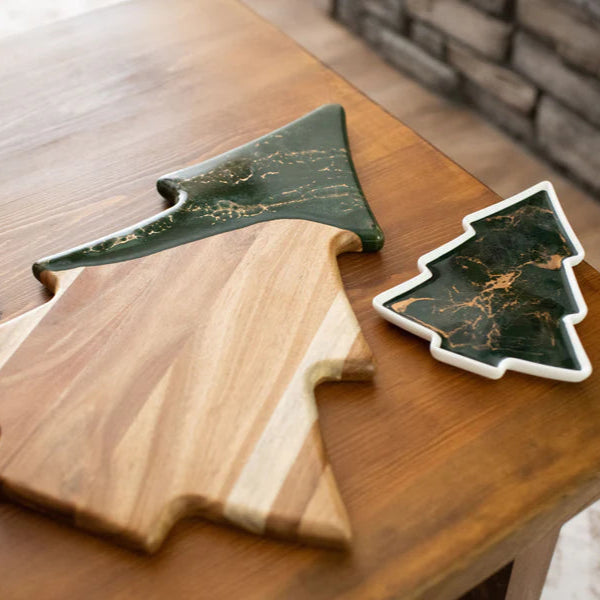 Wooden cutting board shaped like a Christmas tree with a matching green marble-patterned cheese board on a wooden surface.