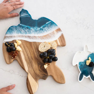 Handcrafted sea turtle-shaped charcuterie board with acacia wood and blue resin accents, topped with fruit and cheese.