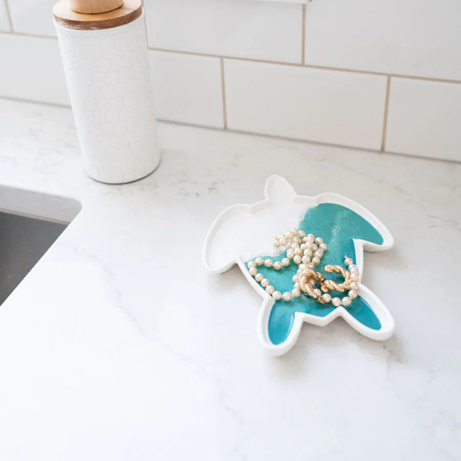 Teal and white resin turtle jewelry dish on a kitchen counter with a soap dispenser in the background.